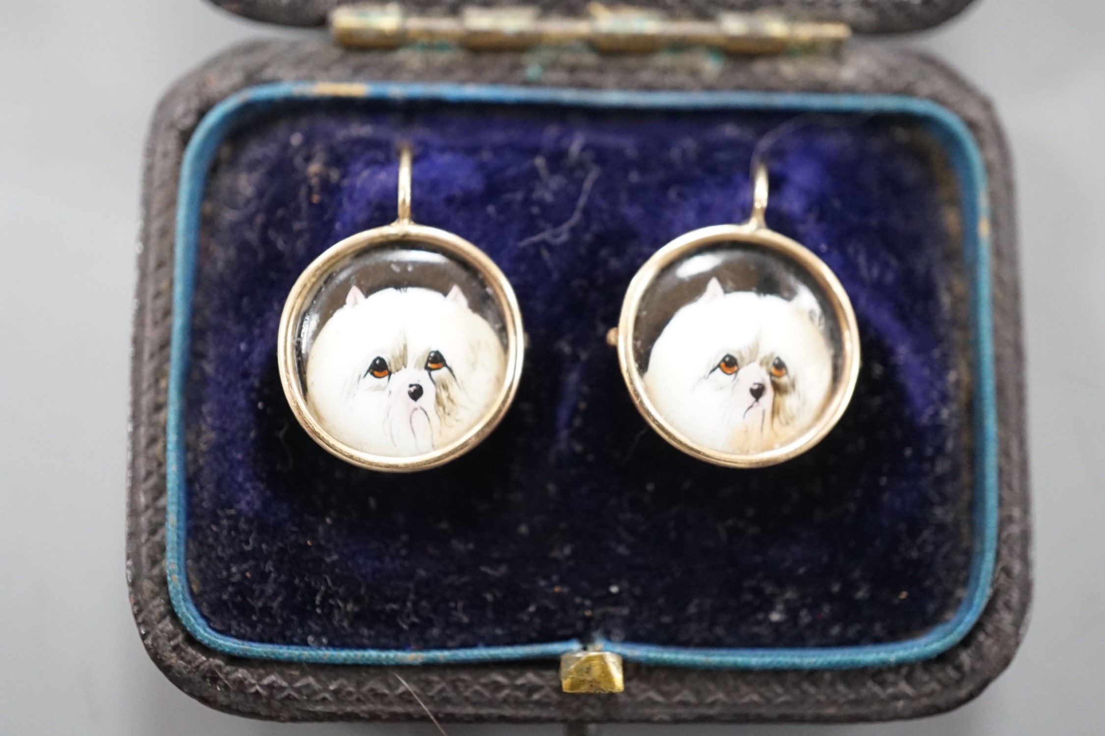 A cased pair of yellow metal and circular enamel earrings, decorated with the heads of a dog, diameter 14mm, gross weight 2.8 grams.